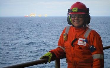 Woman wearing orange boiler suit, safety helmet and safety glasses with North Sea behind her